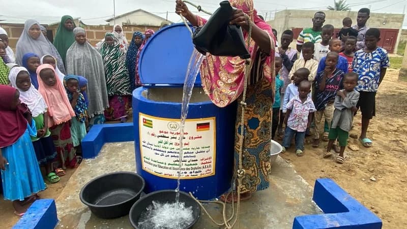 Frau schöpft Wasser am Brunnen — Kinder schauen zu
