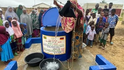 Wasser fließt — Frau schöpft am Brunnen